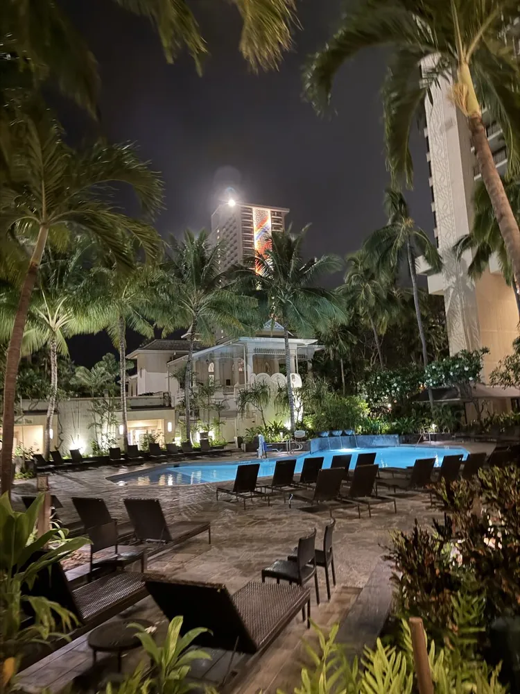 A resort pool lit up at night between palm trees